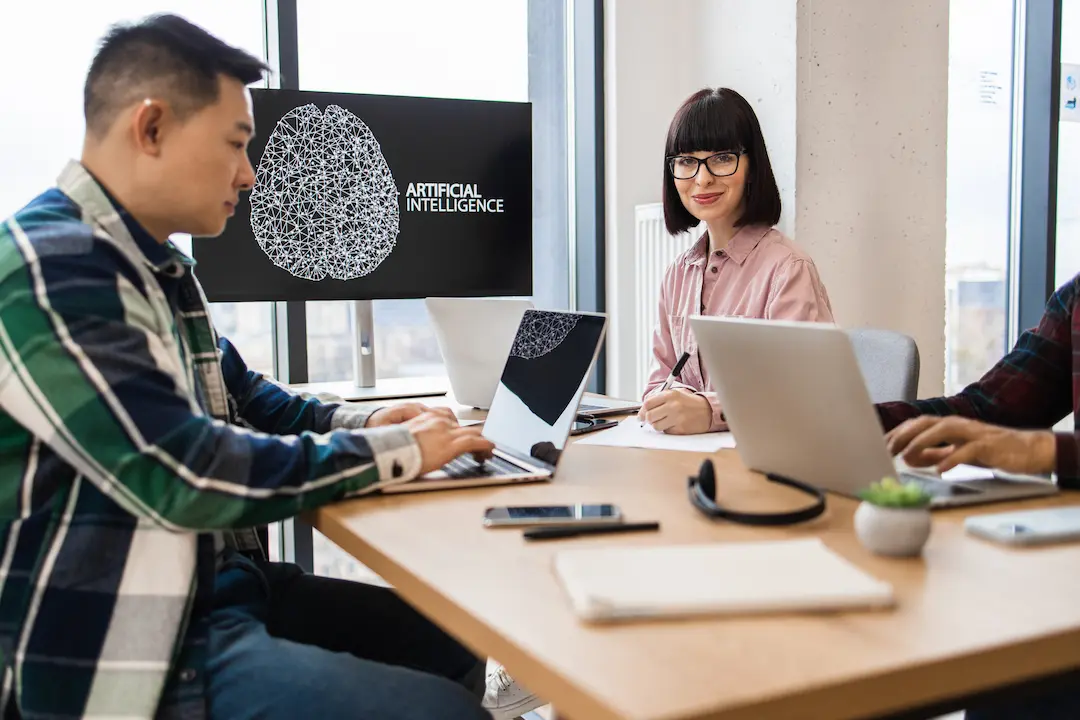 Team arbeitet an Laptops vor einem Bildschirm mit der Aufschrift „Artificial Intelligence“.