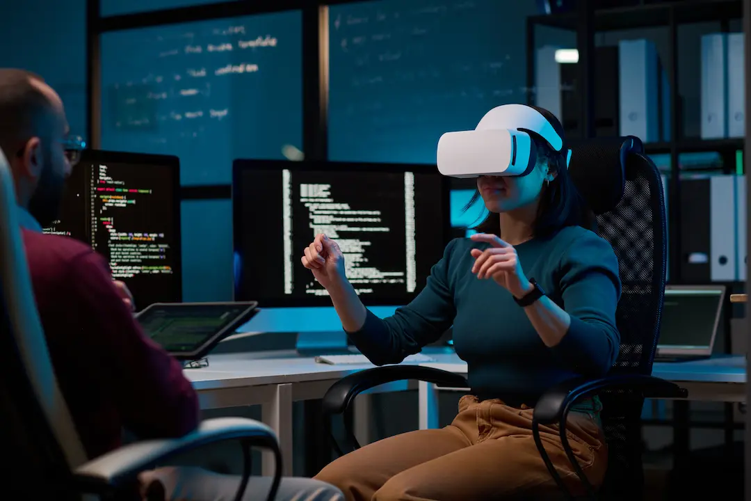 Frau nutzt VR-Headset in einem Büro mit Programmierbildschirmen.