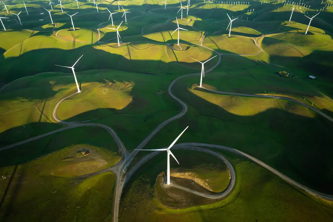 Luftaufnahme eines Windparks mit vielen Windrädern auf grünen Hügeln