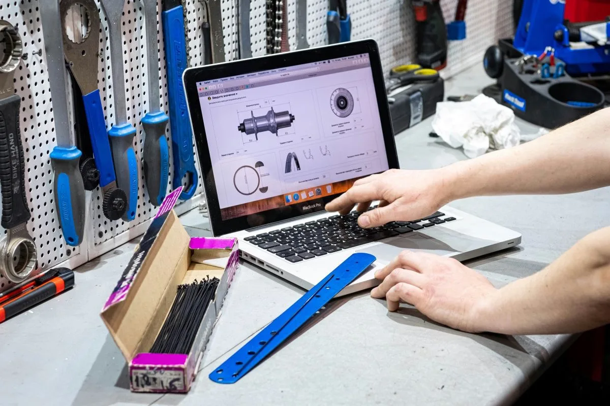 Person arbeitet an einem aufgeklappten Laptop mit technischen Zeichnungen auf dem Bildschirm in einer Werkstattumgebung – steht für ingenieurtechnische Anwendung von KI-Methoden.